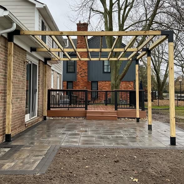 Pressure-treated wood pergola with black metal post brackets over a paver patio, adjacent composite deck with brown decking and black aluminum railing on a brick home, deck building project in Edison, New Jersey